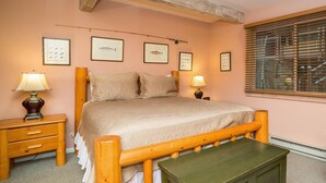Une chambre à coucher avec un lit en bois, deux tables de chevet avec des lampes, une commode verte et des tableaux représentant des poissons, accrochés au mur.