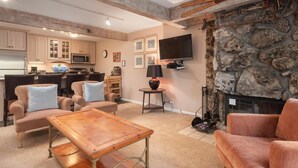 Un vaste salon doté d’une cheminée en pierre, d’un téléviseur fixé au mur et d’un coin salon confortable avec une table basse.