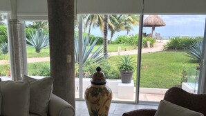 Una habitación amplia con un ventanal grande, un sofá blanco, un sillón de mimbre y un jarrón decorativo.