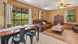 A room with a wooden dining table, two chairs, a sofa, a cabinet, and a ceiling fan. - The Enchanted — A Quiet Riverside Retreat in the Heart of the Ouachita (Pencil Bluff)
