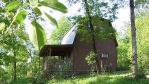 A rustic wooden cabin with a sloped roof, surrounded by lush greenery and trees. - The Enchanted — A Quiet Riverside Retreat in the Heart of the Ouachita (Pencil Bluff)