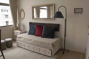 Ein Schlafzimmer mit Bett, Nachttisch, Lampe, Spiegel und einem Fenster mit Vorhängen.