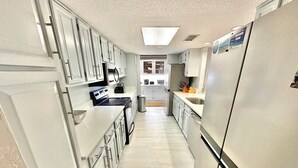 A narrow kitchen with white cabinets, a stainless steel refrigerator, and a microwave.