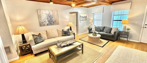 Un salon avec un plafond en bois, un ventilateur de plafond, un ensemble de canapés, une table basse et un tapis.