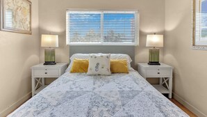 A bedroom with a large bed, two bedside tables, two lamps, and a window with blinds. - Relaxing 1 Bedroom Garden Apartment steps to the Ocean - Best part of the beach! (Hollywood)
