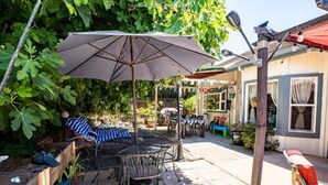 An outdoor patio with a table and chairs, a large umbrella, and a wooden fence. - Ione Captains Cottage With 3 separate BEDROOMS Close to Town. Centrally located. (Ione)