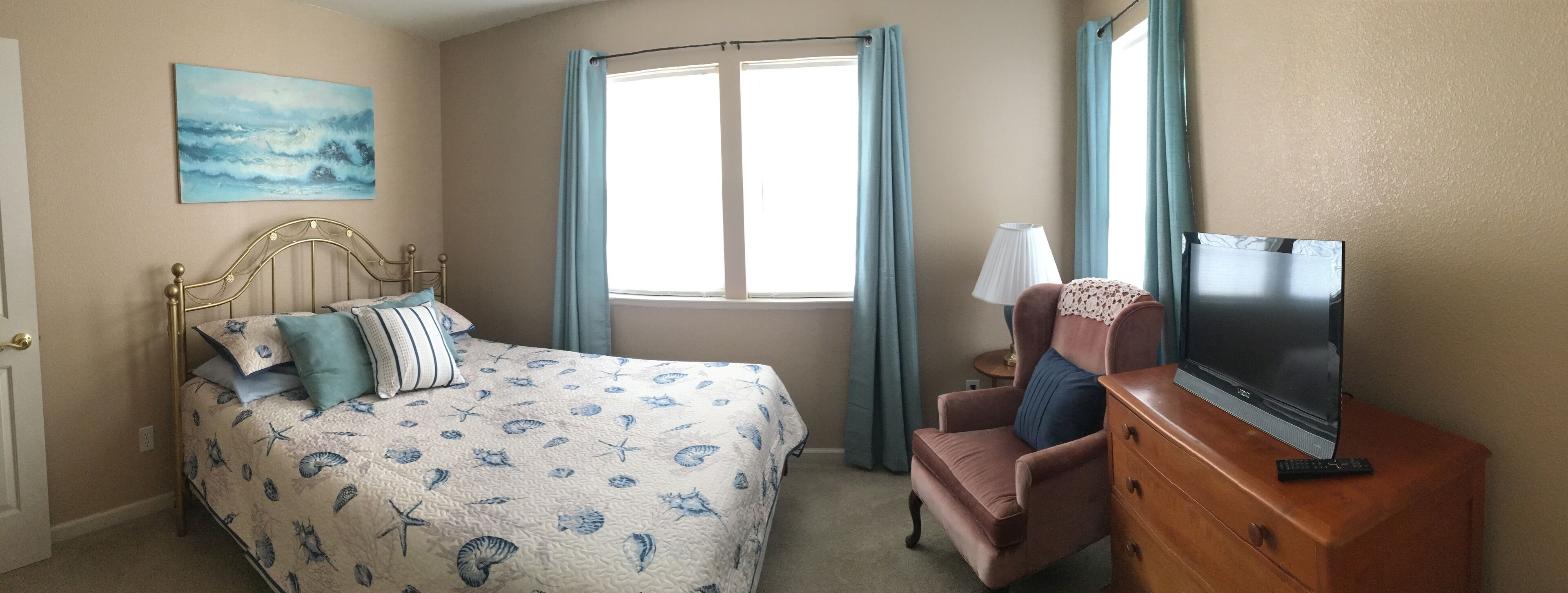 A bedroom with a bed, a TV on a dresser, a chair, and a window with curtains.