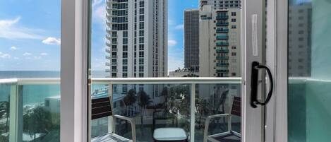 A balcony with a glass door, two chairs, and a view of tall buildings and a body of water.