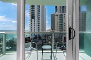 A balcony with a glass door, two chairs, and a view of tall buildings and a body of water.