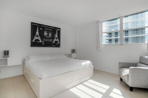 Un dormitorio moderno con cama, una silla, un ventanal y una obra de arte colgada en la pared.