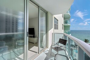 A balcony with a glass door leading to a room with a TV, a chair, and a small table.