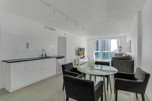 A modern kitchen with white cabinets, a black countertop, and a glass dining table with four chairs.