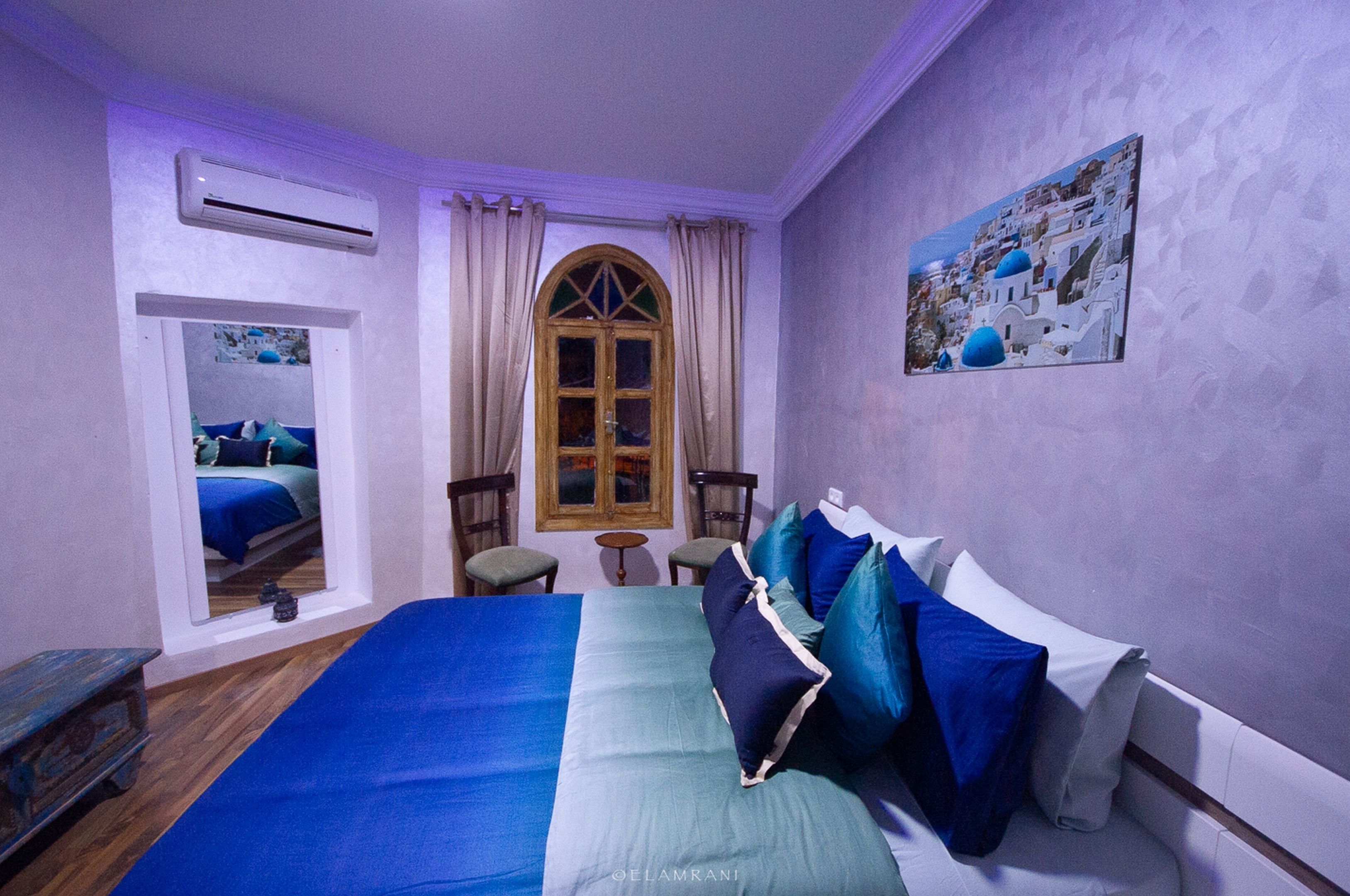 A bedroom with a large bed, two chairs, a small table, and a window with curtains.