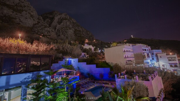 A nighttime view of a coastal town with buildings, a pool area, and a mountain backdrop. - Hotel Ziryab (Chefchaouen)