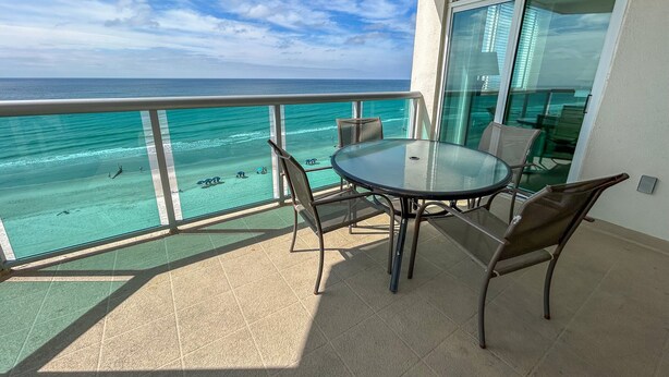 Ein Balkon mit Glastisch und Stühlen mit Blick auf Strand und Meer.