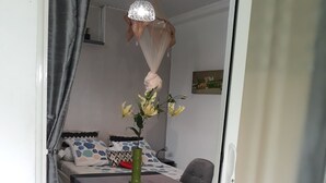 A room with a dining table, chairs, a vase with flowers, a bed with patterned bedding, and a hanging light fixture.