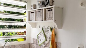 A kitchen with a sink, a window with plants, and a shelf with kitchen items.