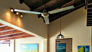 Une cuisine avec des meubles en bois, un plan de travail en marbre, un ventilateur de plafond et des œuvres d’art accrochées aux murs.