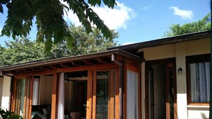 Un espace extérieur abrité, doté d’une pergola en bois, d’un coin salon avec une table et des chaises, et offrant une vue sur un bâtiment avec de grandes fenêtres et une porte.