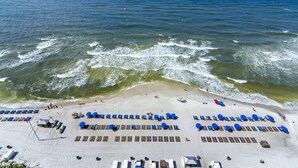 Luchtbeeld van een strand met rijen ligbedden en parasols, een zandstrand en de oceaan.