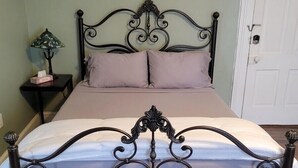 A bed with a dark metal frame and a white mattress, a bedside table with a lamp, and a door in the background.