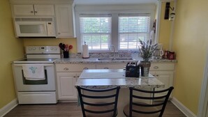 A kitchen with white cabinets, a microwave, an oven, a sink, and two bar stools.