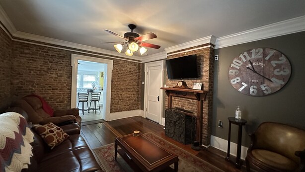 A living room with a brick wall, a fireplace, a large clock, and a leather sofa.