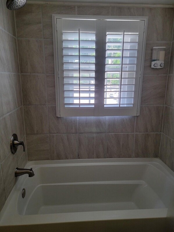 A bathroom with a bathtub, a window with blinds, and a hand dryer.