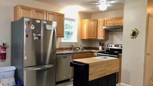 A compact kitchen with wooden cabinets, a stainless steel refrigerator, a dishwasher, and a small island with a sink. - Bungalow by the Bay (Villas)