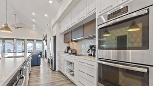 A modern kitchen with stainless steel appliances, white cabinetry, and a large island with seating. - 5410- Ocean Star - Oceanfront Nags Head Luxury Home w/ Pool (Nags Head)