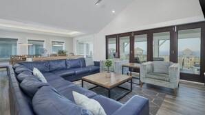 A spacious living area with a large sectional sofa, a coffee table, and a patterned armchair. - 5410- Ocean Star - Oceanfront Nags Head Luxury Home w/ Pool (Nags Head)