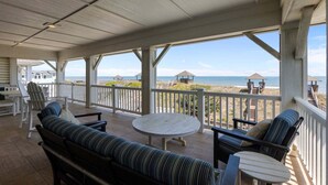 A covered outdoor area with a view of the beach, furnished with a sofa, chairs, and a table. - 5410- Ocean Star - Oceanfront Nags Head Luxury Home w/ Pool (Nags Head)