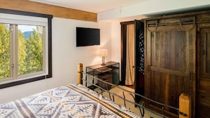 A bedroom with a bed, a TV mounted on the wall, a window with a view of trees, and a wooden wardrobe. - Teton Village 3.5BR/2.5BA  - Walking Distance to Ski Lifts! (Jackson)