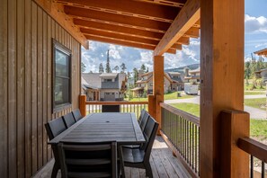 Une terrasse en bois avec une table et des chaises, donnant sur un quartier résidentiel avec des maisons et des arbres.