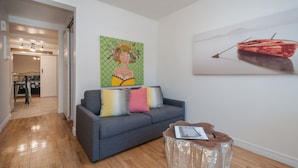 A modern living room with a grey sofa, colorful cushions, a wooden coffee table, and two paintings on the walls. - ESPACE COURONNE QUEBEC (La Cité-Limoilou)