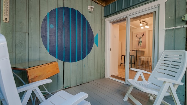 A wooden deck with white plastic chairs, a wooden table, and a glass door leading to an interior space with a chandelier and a deer head decoration. - ESPACE COURONNE QUEBEC (La Cité-Limoilou)