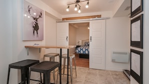 A compact kitchen with a wooden table, two stools, and a painting of a deer. - ESPACE COURONNE QUEBEC (La Cité-Limoilou)