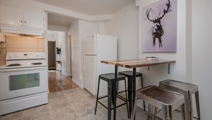 A modern kitchen with white appliances, a wooden table, and two stools. - ESPACE COURONNE QUEBEC (La Cité-Limoilou)