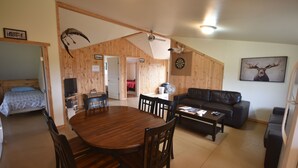 Amplia sala de estar con una mesa de comedor de madera, sofá de cuero negro y dardos.