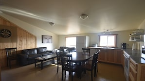 Amplia sala de estar con mesa de comedor, sillas, sofá y cocina con gabinetes de madera y refrigerador.