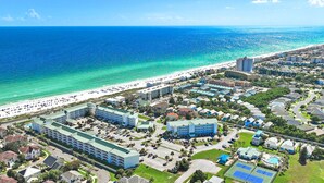 Vista aérea de una zona turística costera con playa, edificios de hotel y piscina.