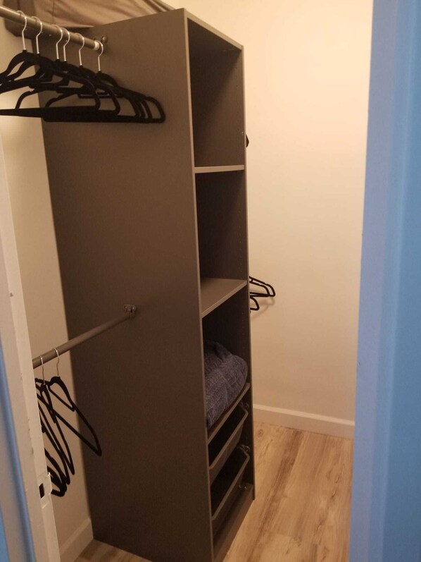 A walk-in closet with a metal rod for hanging clothes, a shelf with folded clothes, and a wooden floor.