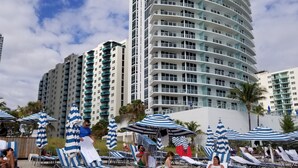 A poolside area with sun loungers and striped umbrellas, surrounded by tall residential buildings. - Beautiful Ocean-View, 16th floor, apartment, right ON THE Beach.  (Hollywood)