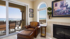 A spacious living room with a leather armchair, a fireplace, and a large window overlooking a beach. - Gulf Front Luxury - Private Elevator/5 Master bdrms - each w/private bath  (Navarre)