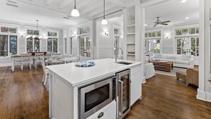 Una cocina amplia con armarios blancos, una isla central y un comedor con sillas blancas.