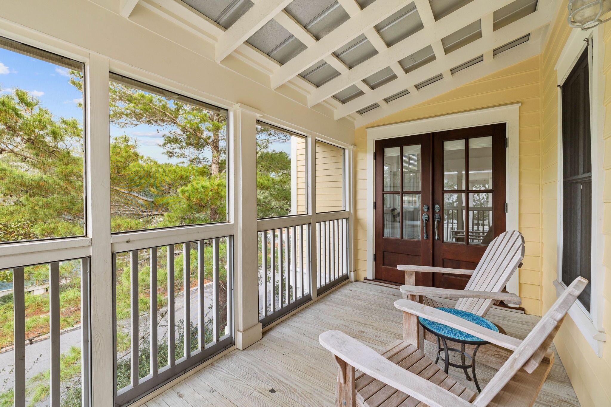 A covered porch with wooden railings, a table with chairs, and a door with glass panels.