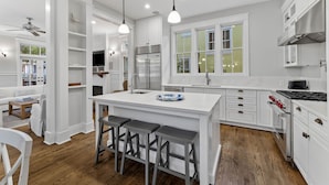 Una cocina moderna con armarios blancos, una isla central con taburetes y un refrigerador de acero inoxidable, además de una estufa.