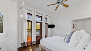Un dormitorio con una cama grande, suelo de madera, ventilador de techo y televisor montado en la pared.