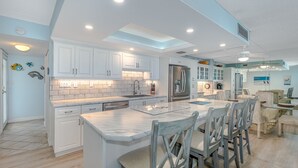 A modern kitchen with white cabinets, a marble island, and a dining area with wooden chairs. - BREATHTAKING OCEAN VIEWS & UPDATED CONDO  (New Smyrna Beach)