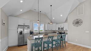Une cuisine moderne avec des meubles blancs, des appareils en acier inoxydable et des chaises de couleur turquoise.